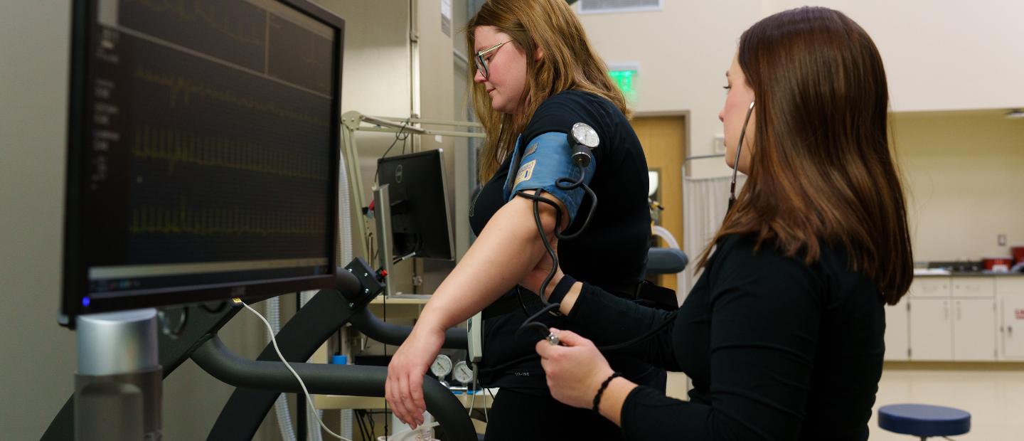 A woman taking another woman's blood pressure on a treadmill.