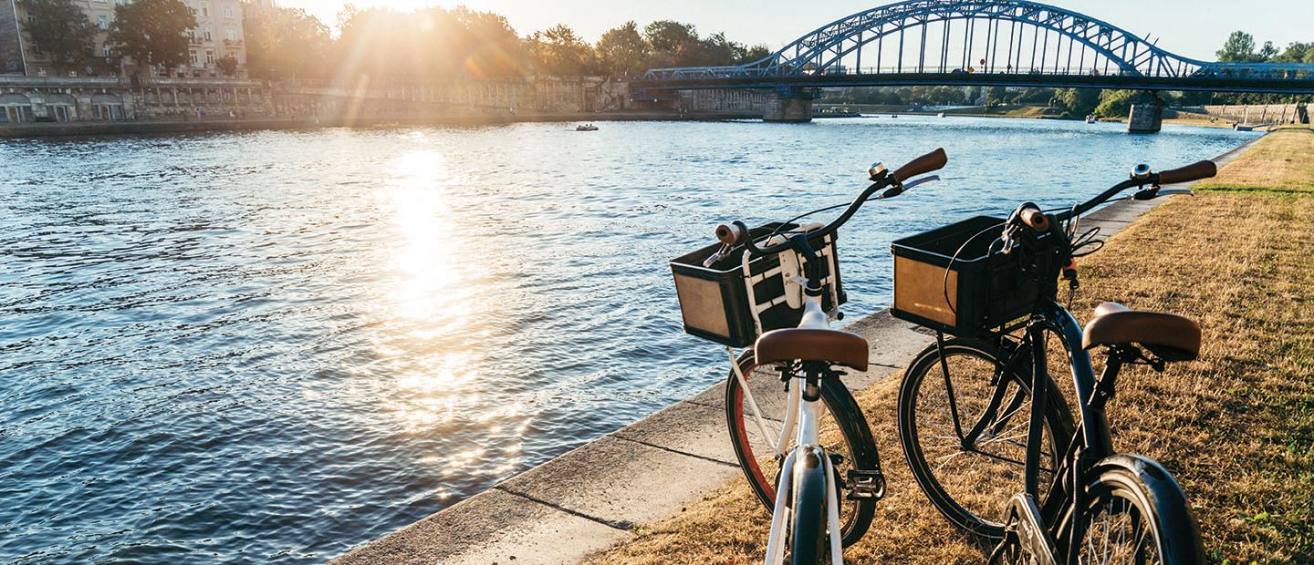 Two bikes parked on grass next to river with bridge in background