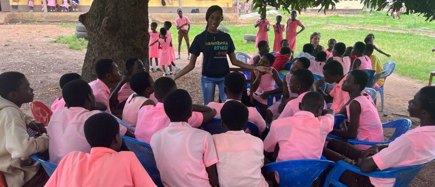 A woman speaking to a group of kids in pink shirts outside.